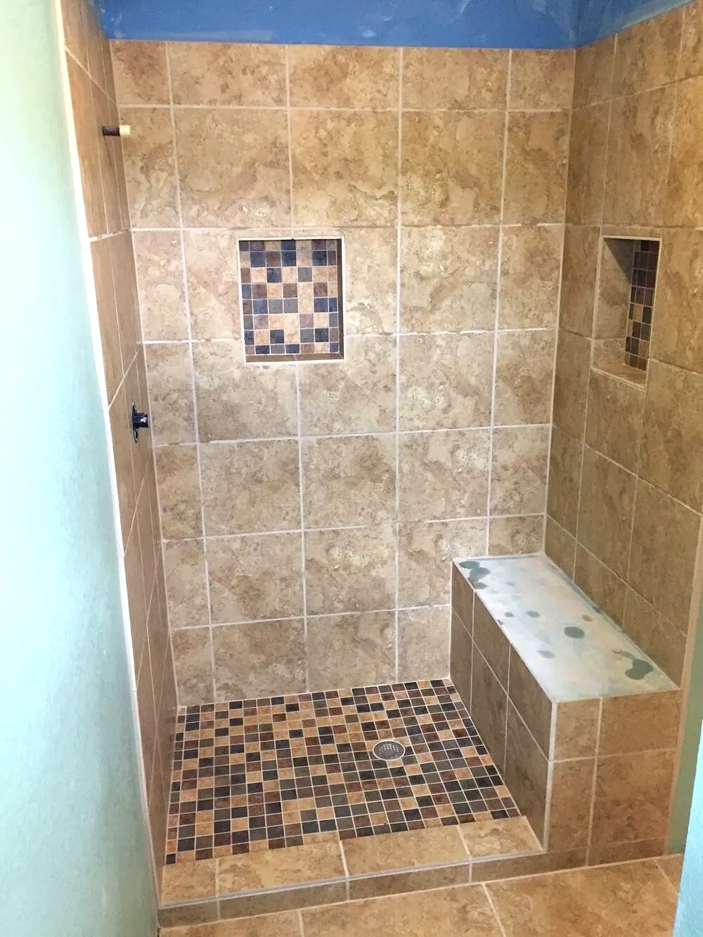 Walk-in tile shower with a mosaic floor, a built-in bench and two recessed niches